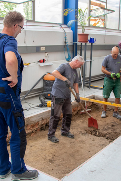 Mitarbeiter graben in einem Werkstattbereich, um ein neues Fundament zu gießen, wo die Klebestreifen waren