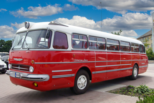 Rot-weißer Oldtimer-Bus des Modells Ikarus Lux steht auf einem Parkplatz bei sonnigem Wetter; das Fahrzeug hat ein gewölbtes Panoramafenster und klassische Rundscheinwerfer.