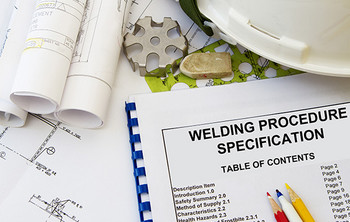 Aufgeschlagenes Dokument mit der Aufschrift „Welding Procedure Specification“, daneben Baupläne, ein weißer Schutzhelm, farbige Bleistifte und technische Zeichnungen.
