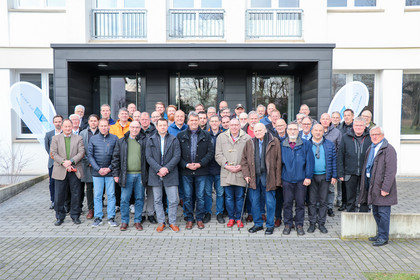 Gruppenfoto von Personen unterschiedlichen Alters vor dem Gebäude der SLV Halle, alle in Winterjacken oder Mänteln, zwei SLV-Flaggen im Hintergrund.