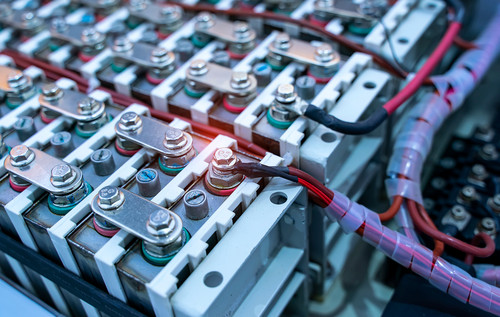Detailaufnahme eines Batterie- oder Akkumoduls mit verschraubten Zellverbindern und roten sowie schwarzen Kabeln, die durch einen Schutzschlauch geführt werden.