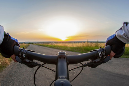 Sicht vom Fahrradlenker auf eine breite Radstraße über Land mit Sonnenaufgang