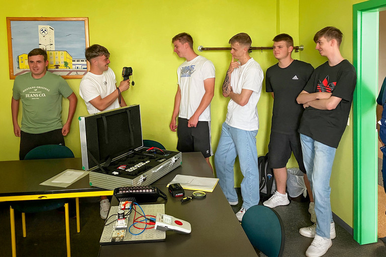 Sechs junge Männer stehen lachend in einem Raum. Einer hält eine Infrarotkamera, vor ihnen steht ein offener Koffer mit Batterie-Equipment auf einem Tisch.