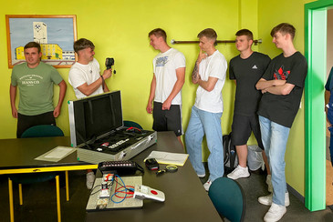 Sechs junge Männer stehen lachend in einem Raum. Einer hält eine Infrarotkamera, vor ihnen steht ein offener Koffer mit Batterie-Equipment auf einem Tisch.
