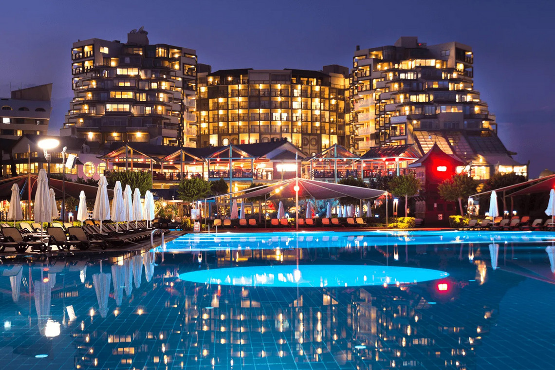 Hotelanlage bei Nacht mit beleuchtetem Gebäude und großem Außenpool im Vordergrund
