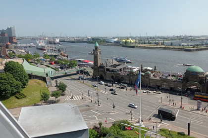 Blick von oben auf die St. Pauli Landungsbrücken in Hamburg, mit Hafengebäuden, Elbe, vorbeifahrenden Schiffen und der Elbphilharmonie im Hintergrund