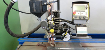 Eine automatisierte UP-Doppeldrahtanlage ist auf einem blauen Werktisch montiert. Die Anlage besteht aus einem Schweißkopf mit Absaugung, Führungsschienen, Drahtvorschub und einem Steuergerät mit Display und Bedienelementen. Auf dem Tisch liegt ein vorbereitetes Werkstück.