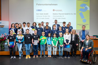 Gruppenfoto der Siegerinnen und Sieger des Regionalwettbewerbs Jugend forscht 2025 in Halle vor der Präsentationsfolie der Patenunternehmen. Die Vertreter der SLV Halle GmbH und Elektrothermit sind mit dabei sowie der Oberbürgermeister Halle. 