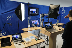 Streaming-Studio mit mehreren Laptops, Kameras, Softboxen und Monitoren vor blauen GSI SLV-Trennwänden, auf den Bildschirmen ist ein Gruppenfoto zu sehen.