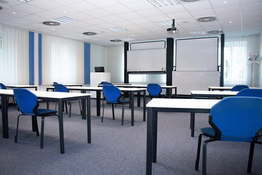 Moderner heller Seminarraum mit Beamer, Whiteboard und blauen Sitzmöbeln