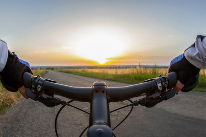 Sicht vom Fahrradlenker auf eine breite Radstraße über Land mit Sonnenaufgang