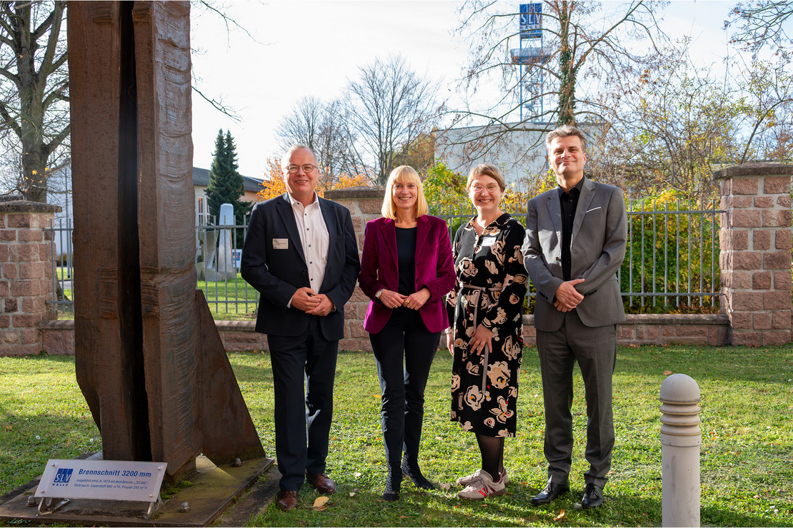 Vier Personen stehen im Freien nebeneinander vor einem Brennschnittrekord. Zwei Männer und zwei Frauen blicken lächelnd in die Kamera, im Hintergrund sind Bäume, eine Wiese und ein Turm mit SLV-Logo zu sehen.