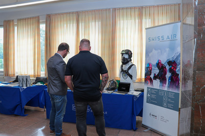 Zwei Männer stehen an einem Ausstellerstand, der mit Informationsmaterialien und einem Exponat dekoriert ist.