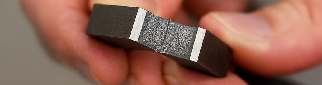 Hand hält ein metallisches Probestück nach einem Kerbschlagversuch