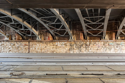 Blick unter eine Stahlbrücke mit genieteter Tragstruktur. Die Konstruktion zeigt historische Elemente und Spuren von Witterungseinflüssen.