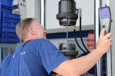 Zwei Mitarbeiter testen Betonstahl auf einer Zugrüfmaschine