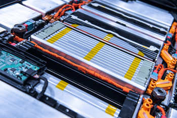 Detailansicht eines geöffneten Batteriepacks mit mehreren flachen Zellmodulen, orangefarbenen Hochvoltkabeln und elektronischen Steuerkomponenten.