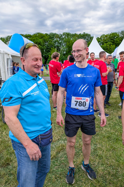 Zwei Männer stehen auf einer Wiese vor Zelten und unterhalten sich, einer trägt ein SLV Halle T-Shirt, der andere ein hellblaues Polo-Shirt.