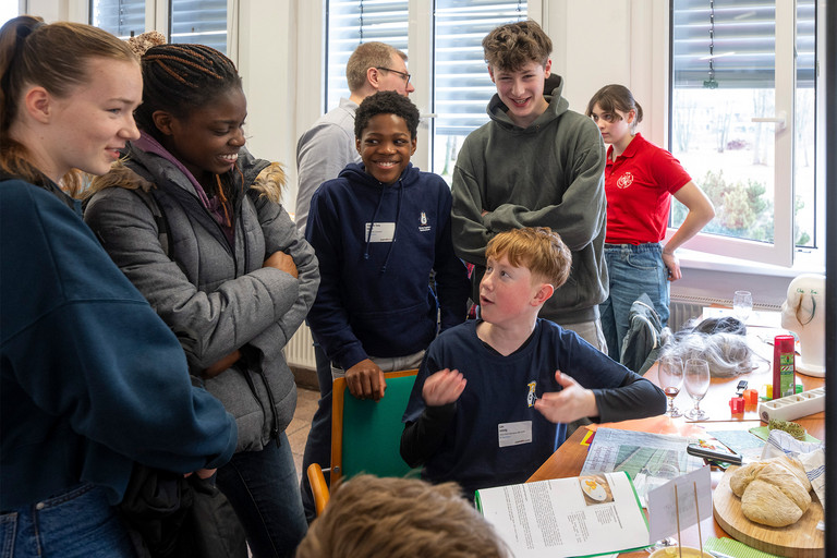 Eine Gruppe Jugendlicher steht um einen Tisch, diskutiert und lacht.