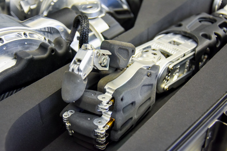 Nahaufnahme einer metallischen Roboterhand mit beweglichen Fingergelenken, schwarzen Gehäuseteilen und sichtbaren Schraubverbindungen, die in einer Schaumstoffaussparung liegt.