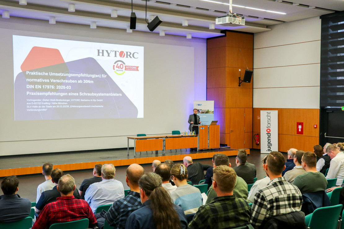 Vortrag in einem Hörsaal mit zahlreichen Teilnehmenden, eine Präsentation wird auf großer Leinwand gezeigt, vorne steht eine sprechende Person