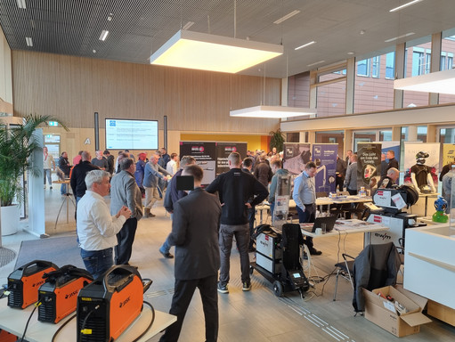 Blick in das Foyer einer Fachmesse mit zahlreichen Besuchenden an Ständen zu Schweißtechnik und Industrieanwendungen, im Vordergrund verschiedene EWM-Schweißgeräte.