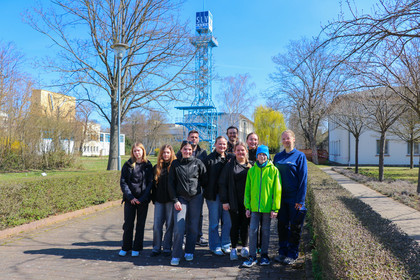 Gruppenfoto von sieben Mädchen, einem Jungen und drei Betreuenden im Außenbereich der SLV Halle bei sonnigem Wetter, im Hintergrund der SLV-Turm.