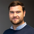 Christoph Gajda, im blauen Hemd, lächelnd vor neutralem Hintergrund