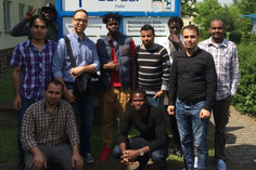 Zehn Männer stehen vor einem Wegweiser mit der Aufschrift „GSI SLV Halle – Haus 1“, im Hintergrund sind Bäume und ein Institutsgebäude zu sehen.