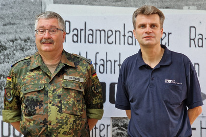 Zwei Männer stehen vor einer historischen Texttafel; der linke trägt eine Tarnuniform der Bundeswehr, der rechte ein dunkelblaues Polohemd mit SLV Halle-Logo.   4/4