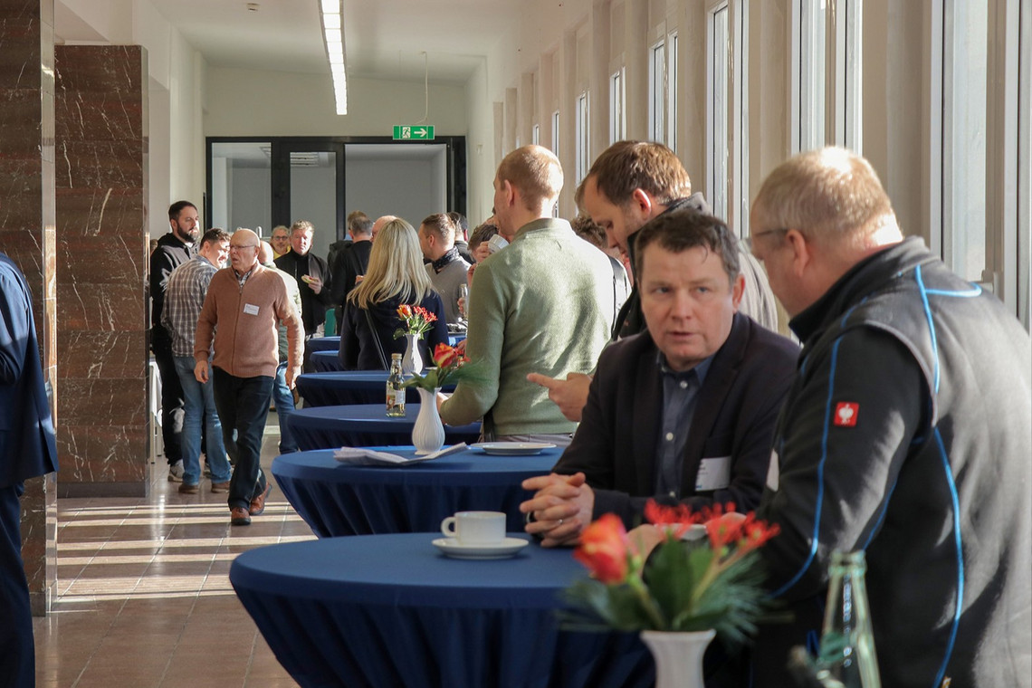 Menschen unterhalten sich an Stehtischen während einer Pause in einem hellen Foyer