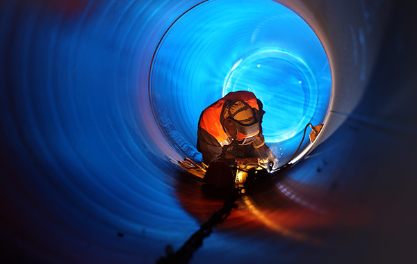 Schweißer mit Schutzkleidung arbeitet im Inneren eines großen Rohres, das von blauem Licht ausgeleuchtet wird.