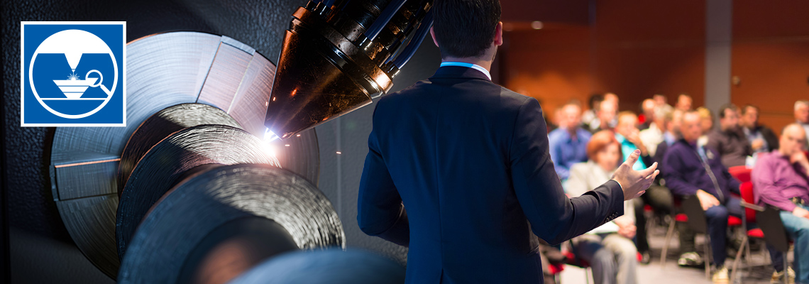 Ein Mann im Anzug hält einen Vortrag vor einem sitzenden Publikum, links daneben eine Detailaufnahme eines Laserauftragsschweißprozesses mit Funkenflug, oben links das Logo der SLV Halle GmbH