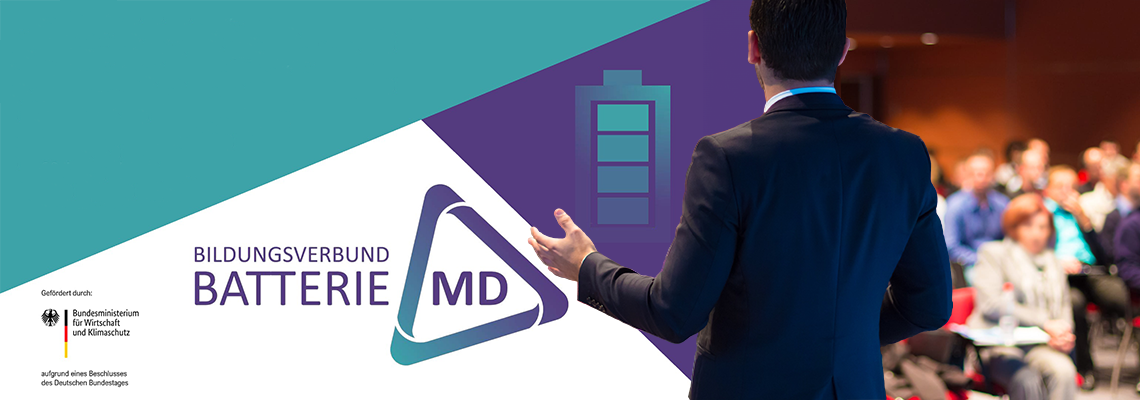 Ein Mann im Anzug spricht vor einem Publikum bei einer Fachveranstaltung; links im Bild befinden sich Titel und Logos des Verbundes „Batterie MD“, ergänzt durch ein stilisiertes Batteriesymbol.
