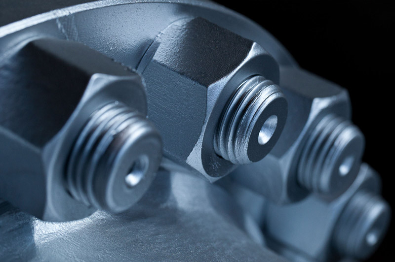 Makroaufnahme mehrerer glänzender Sechskantschrauben mit Feingewinde, die nebeneinander in eine metallische Oberfläche eingeschraubt sind.