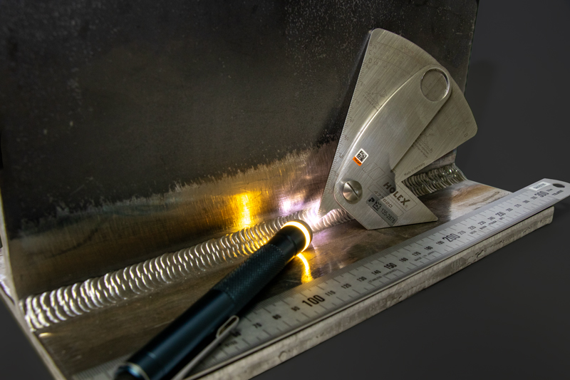 Nahaufnahme einer Schweißnaht, die mit einer Taschenlampe ausgeleuchtet wird, daneben liegt ein Nahtprüfgerät und ein Lineal zur Kontrolle der Geometrie.